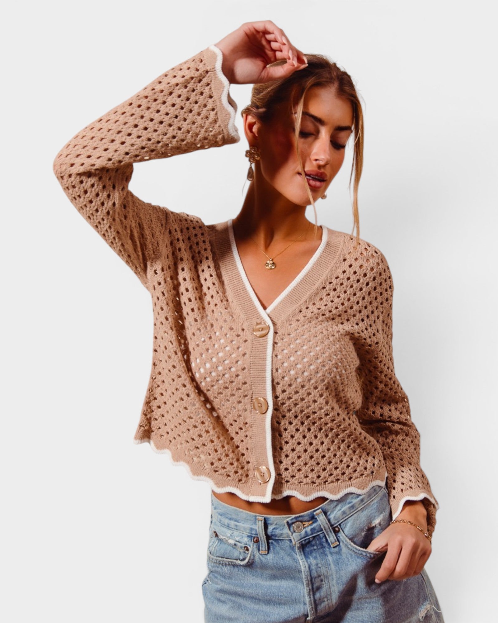 Woman wearing a beige crochet cardigan and denim shorts on a white background