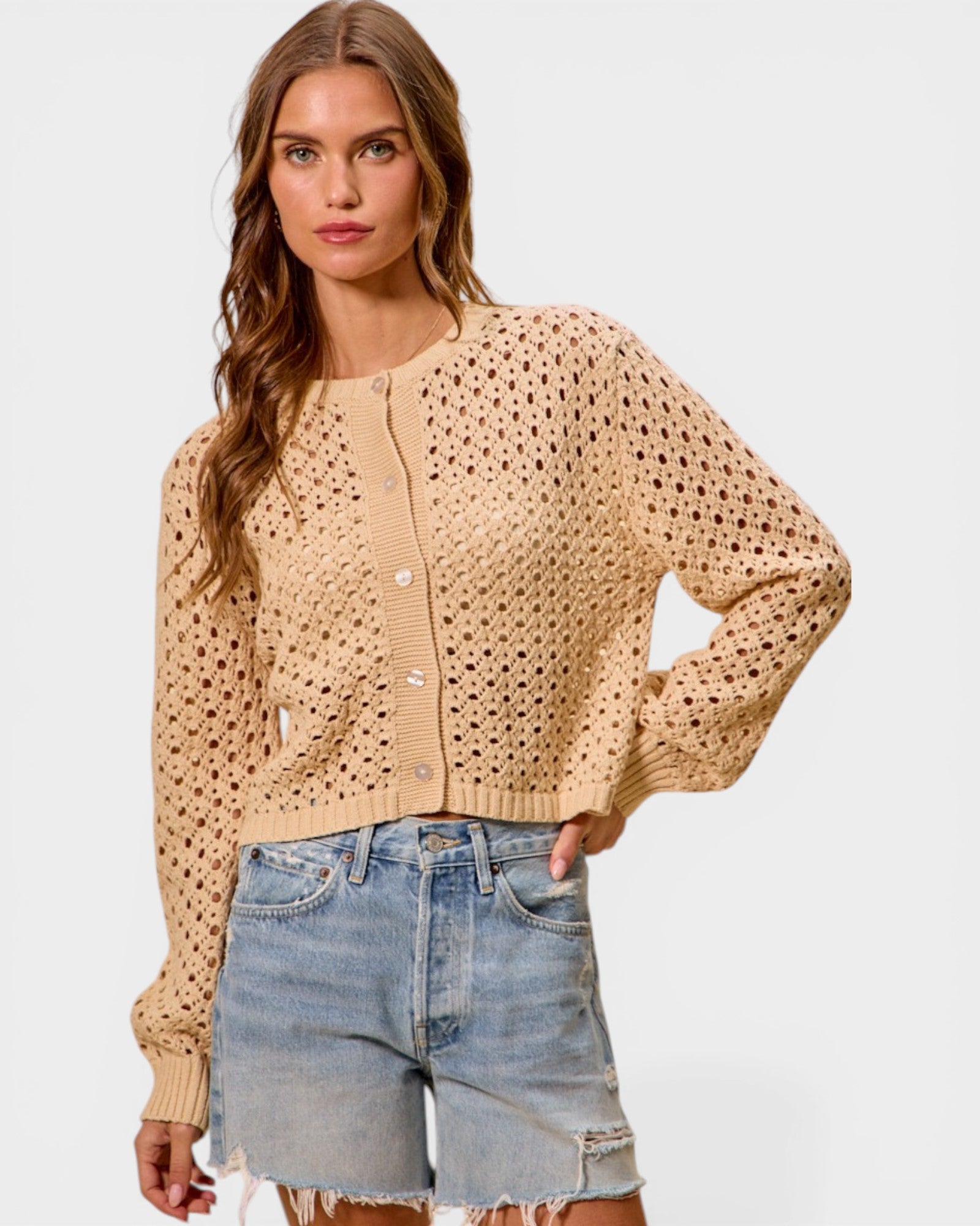 Woman wearing a beige cardigan and denim shorts on a white background