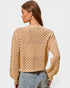 Woman wearing a beige open-knit sweater and jeans on a light gray background