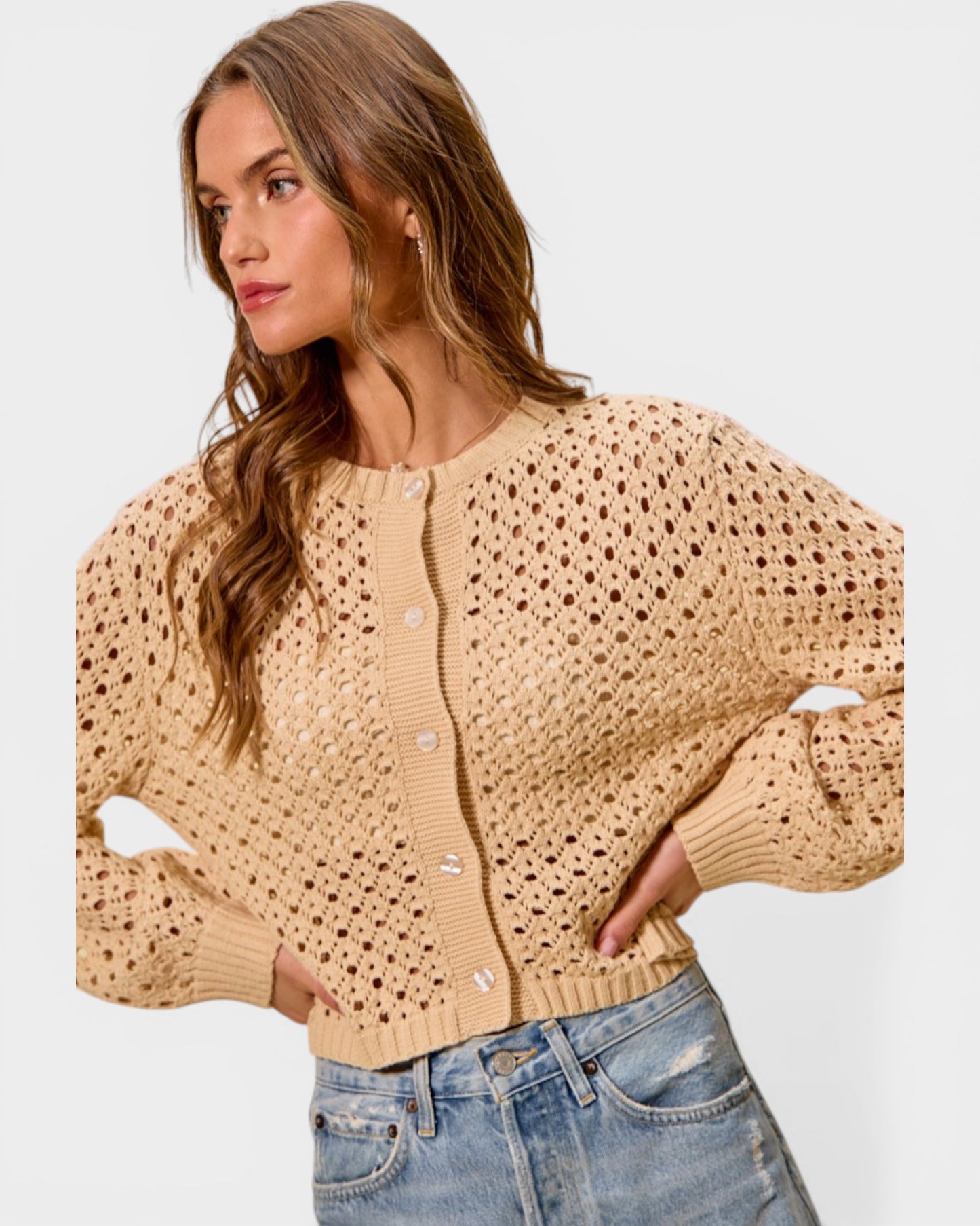 Woman wearing a beige open-knit cardigan and jeans on a light gray background