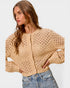 Woman wearing a beige open-knit cardigan and jeans on a light gray background