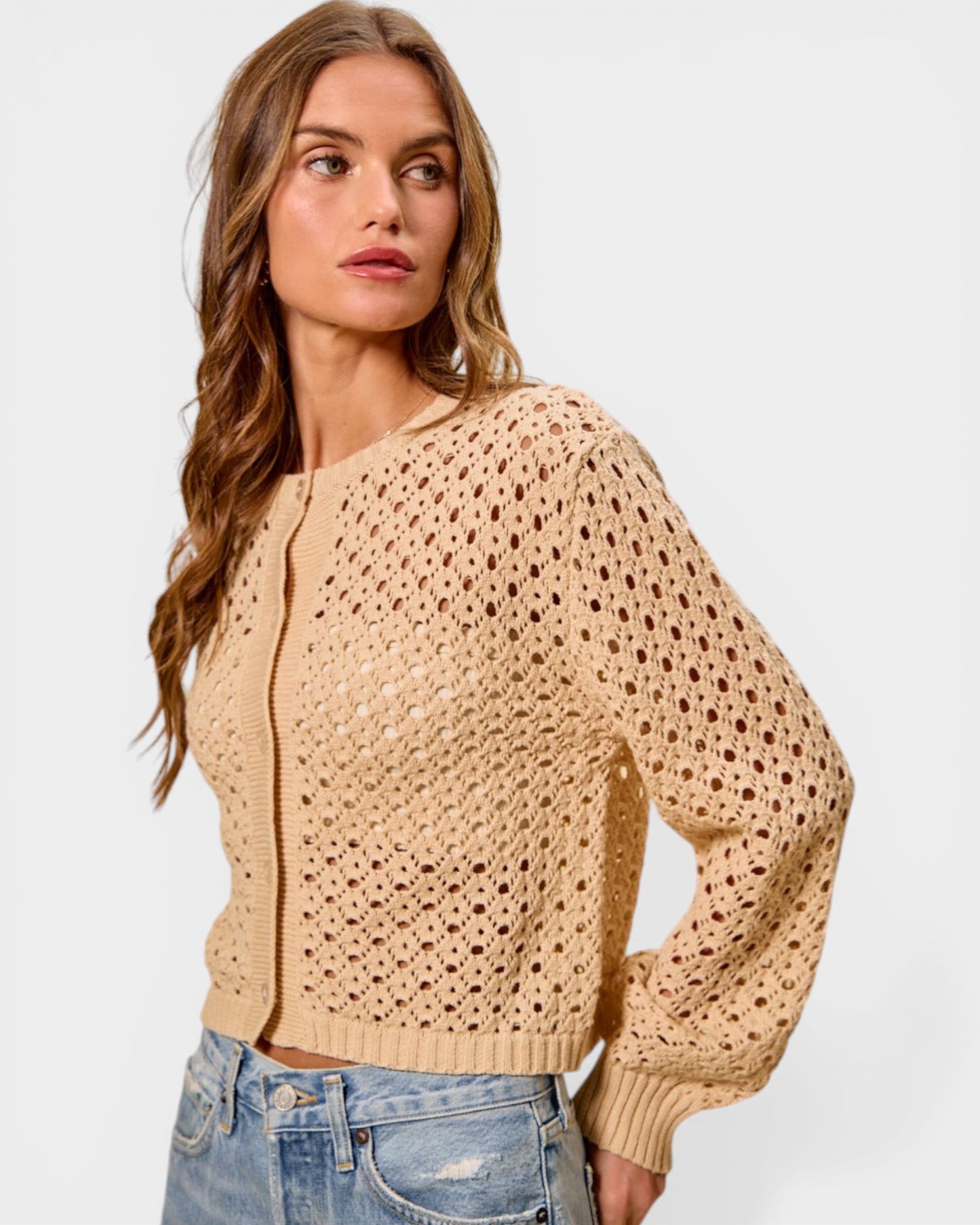 Woman wearing a beige open-knit sweater against a plain background