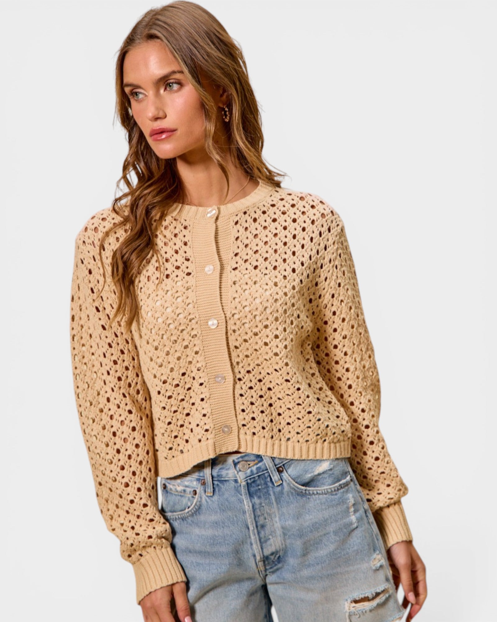 Woman wearing a beige cardigan and jeans on a light gray background