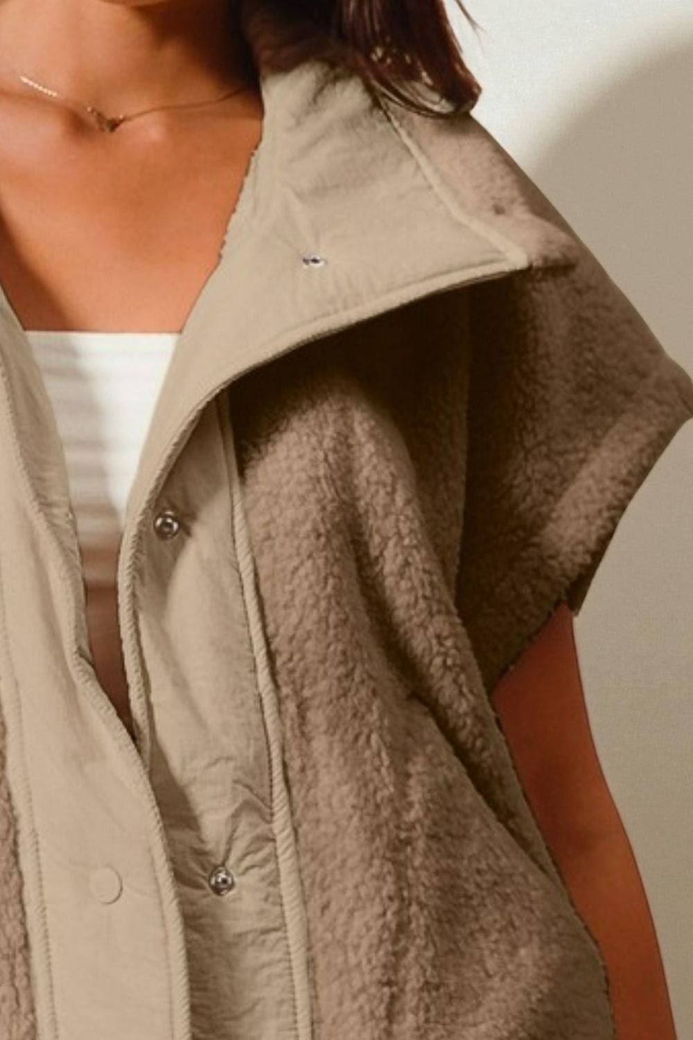 Close-up of a person wearing a beige fleece vest against a neutral background