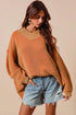 Woman wearing a mustard yellow sweater and denim shorts against a beige background