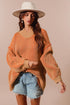 Woman wearing an orange sweater, denim shorts, and a white hat on a beige background