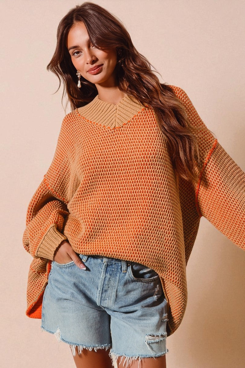 Woman wearing an orange sweater and denim shorts against a beige background