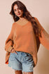 Woman wearing an orange sweater and denim shorts against a beige background