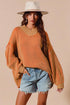 Woman wearing an orange sweater and denim shorts with a beige background