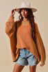 Woman wearing a mustard yellow sweater, denim shorts, and a white hat against a beige background