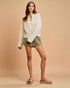 Woman wearing a white lace top and green shorts against a beige background