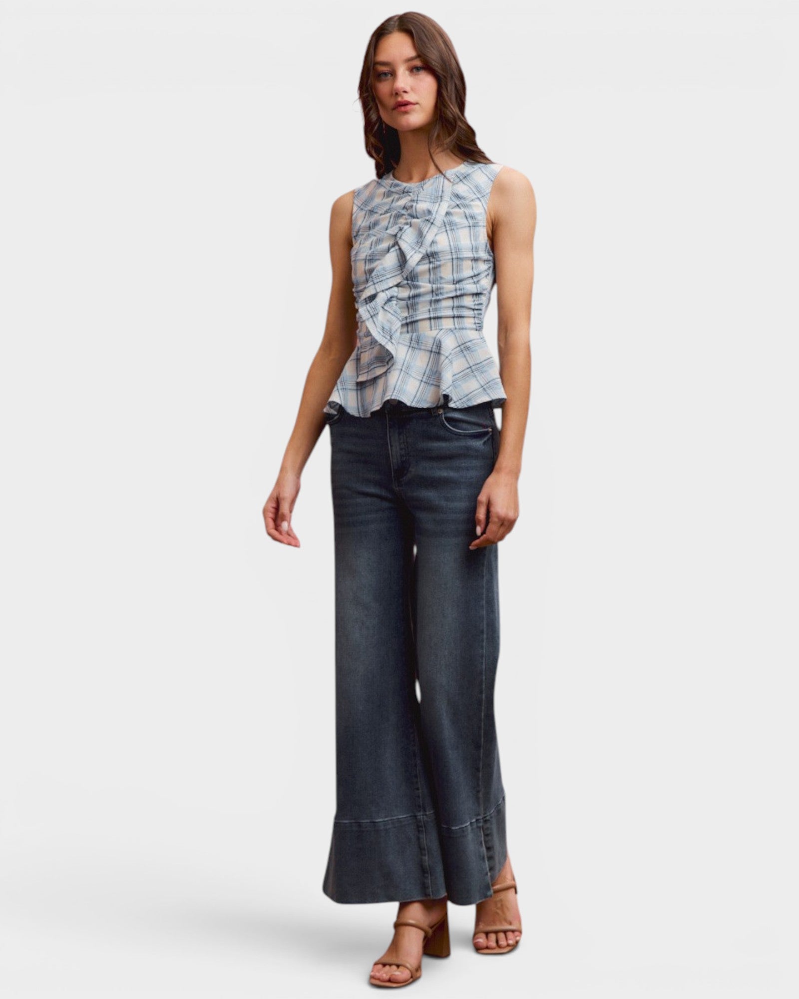 Woman wearing a sleeveless patterned top and wide-leg jeans on a white background