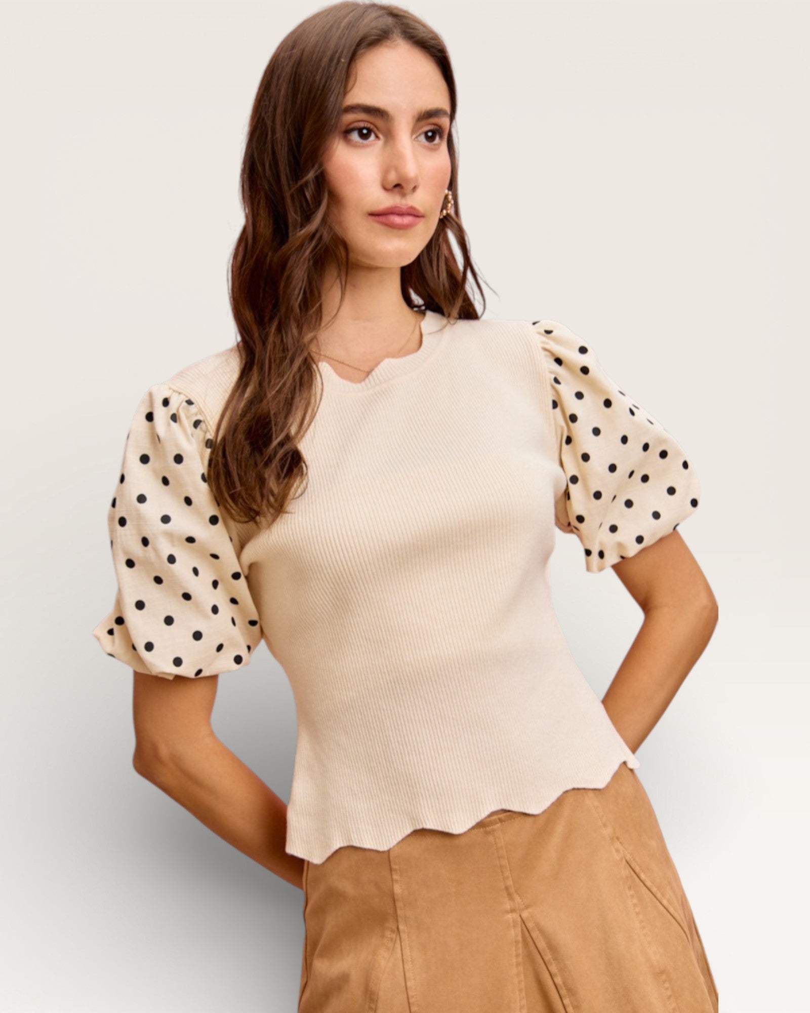 Woman wearing a beige top with polka dot sleeves on a plain background