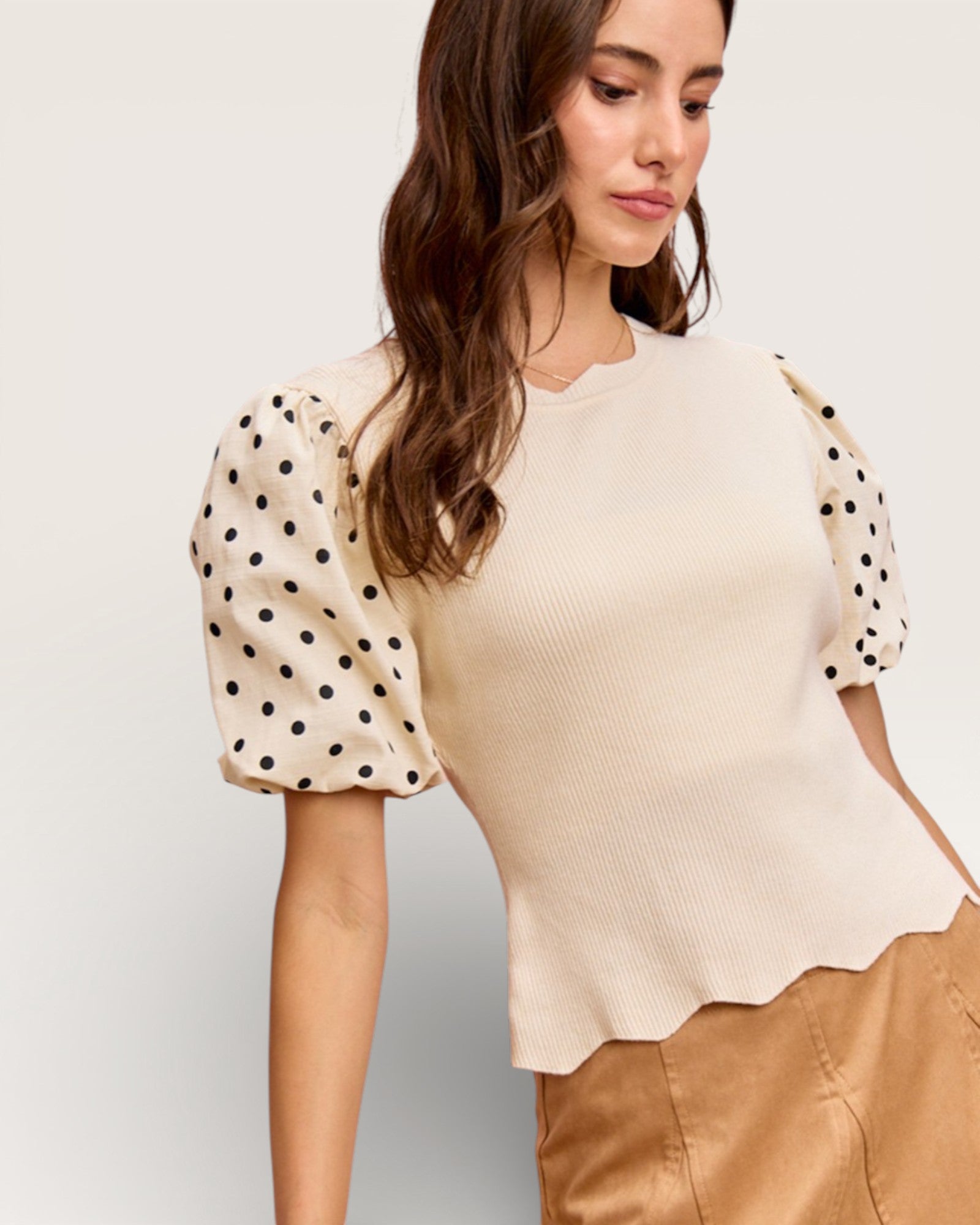 Woman wearing a beige blouse with polka dot sleeves on a plain background