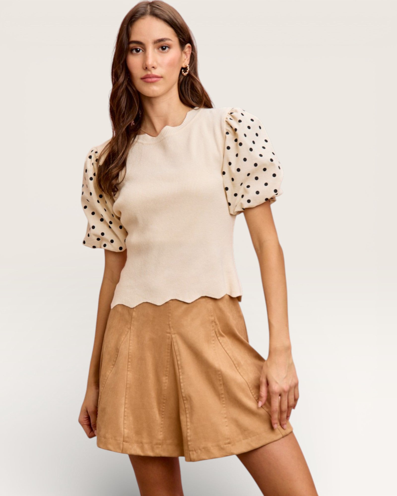 Woman wearing a beige top with polka dot sleeves and a tan skirt on a white background