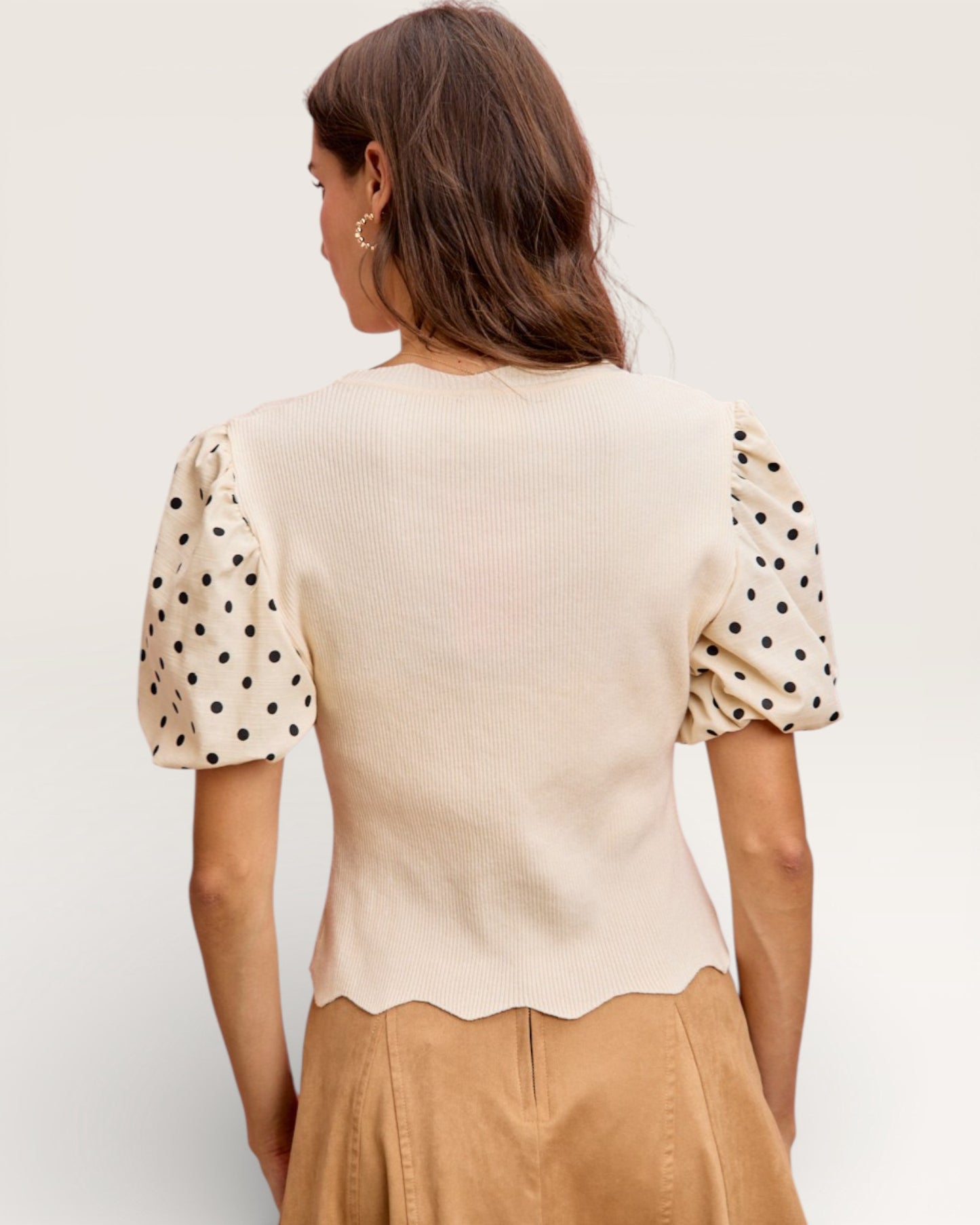 Woman wearing a beige top with polka dot sleeves against a plain background