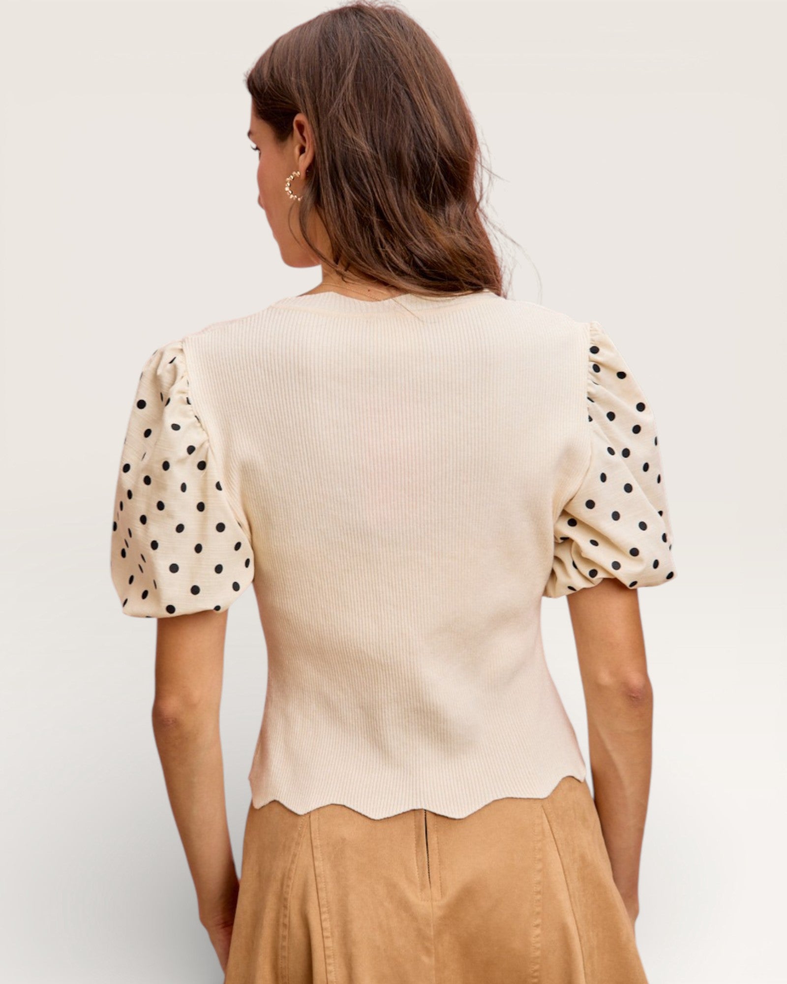 Woman wearing a beige top with polka dot sleeves against a plain background