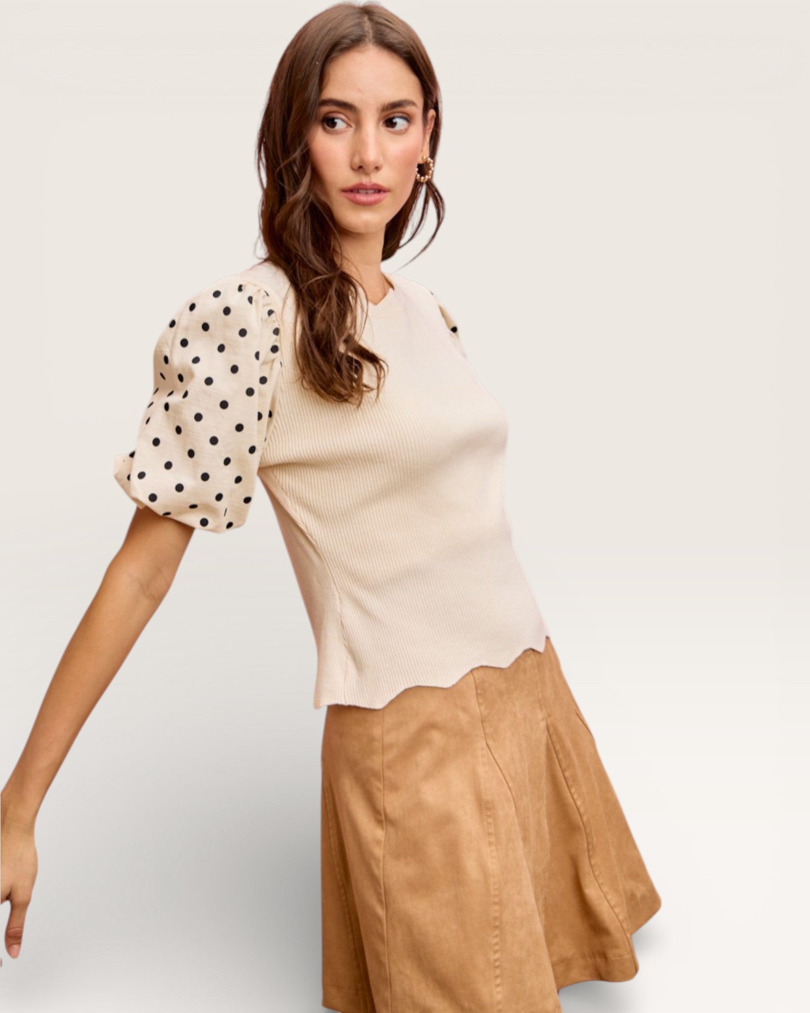Woman wearing a beige top with polka dot sleeves and a brown skirt on a white background