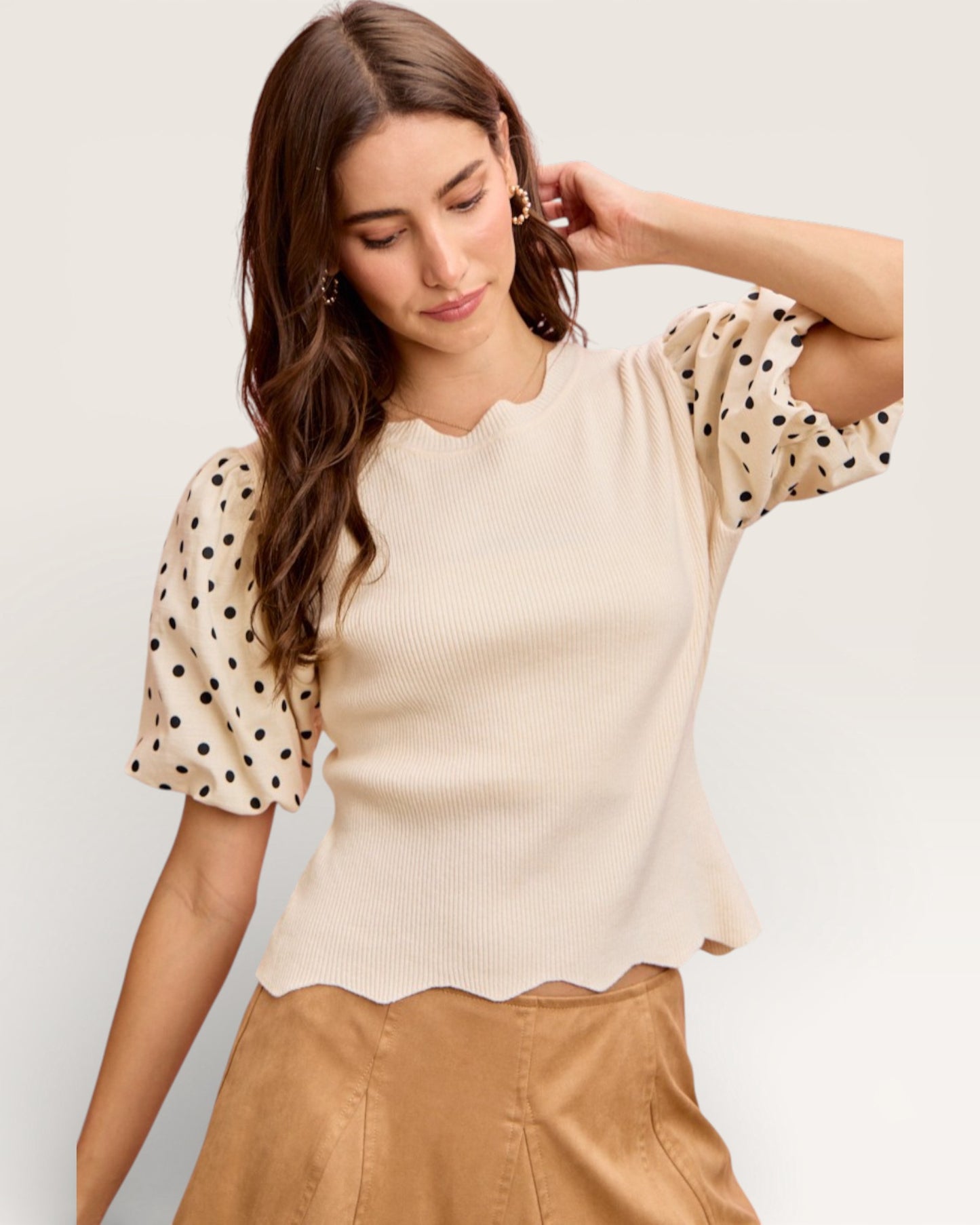 Woman wearing a beige top with polka dot sleeves against a plain background