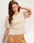 Woman wearing a beige top with polka dot sleeves against a plain background