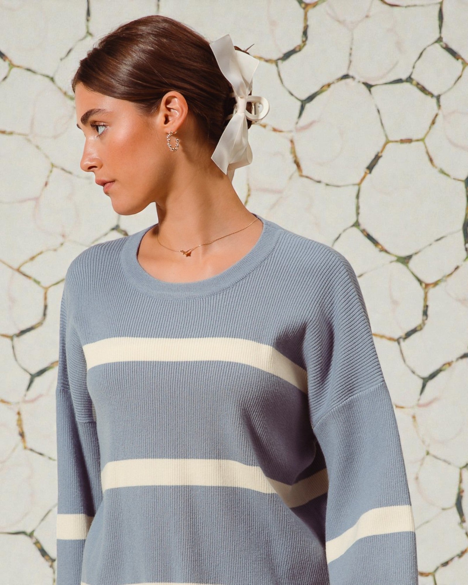 Woman wearing a blue sweater with white stripes against a stone wall background