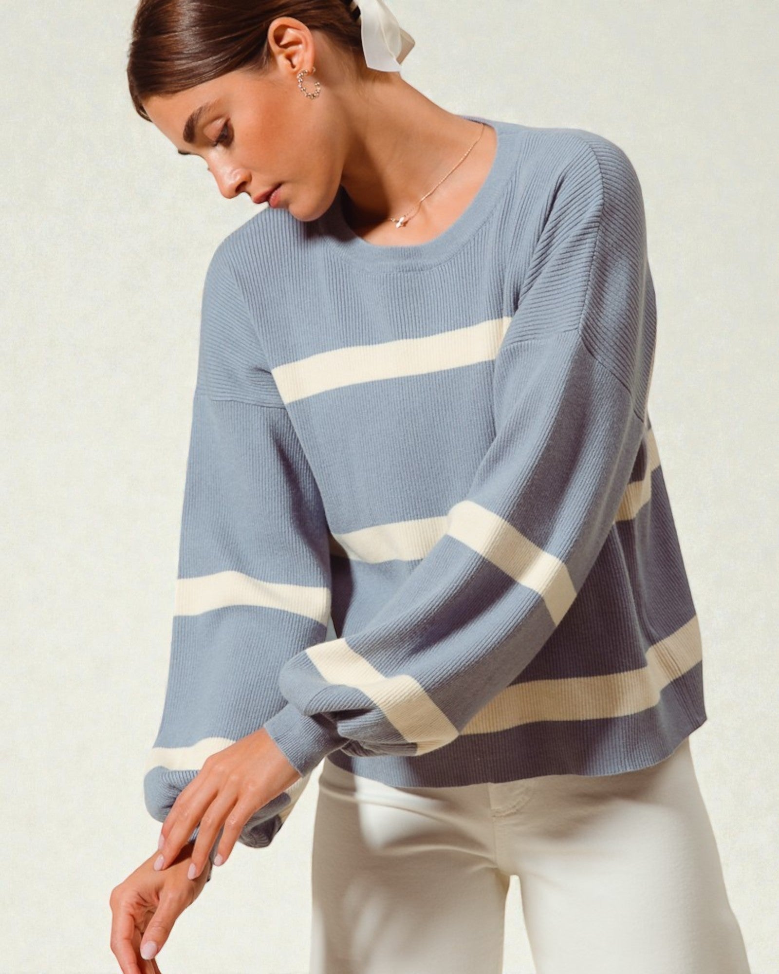 Woman wearing a blue sweater with white stripes on a plain background