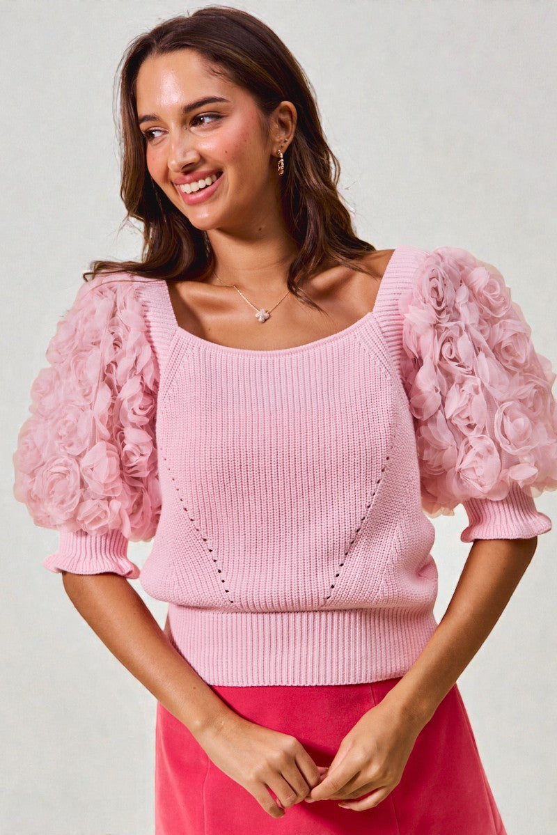 Woman wearing a pink sweater with floral puff sleeves against a plain background