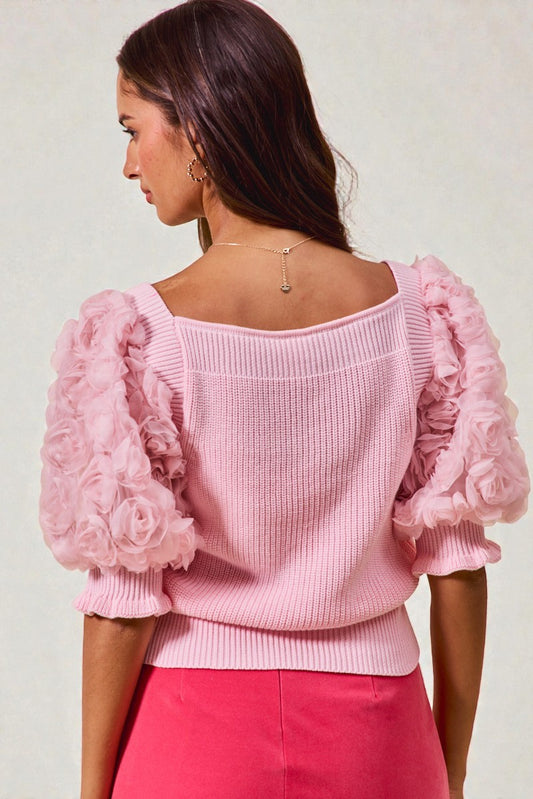 Woman wearing a pink sweater with floral sleeves on a light background