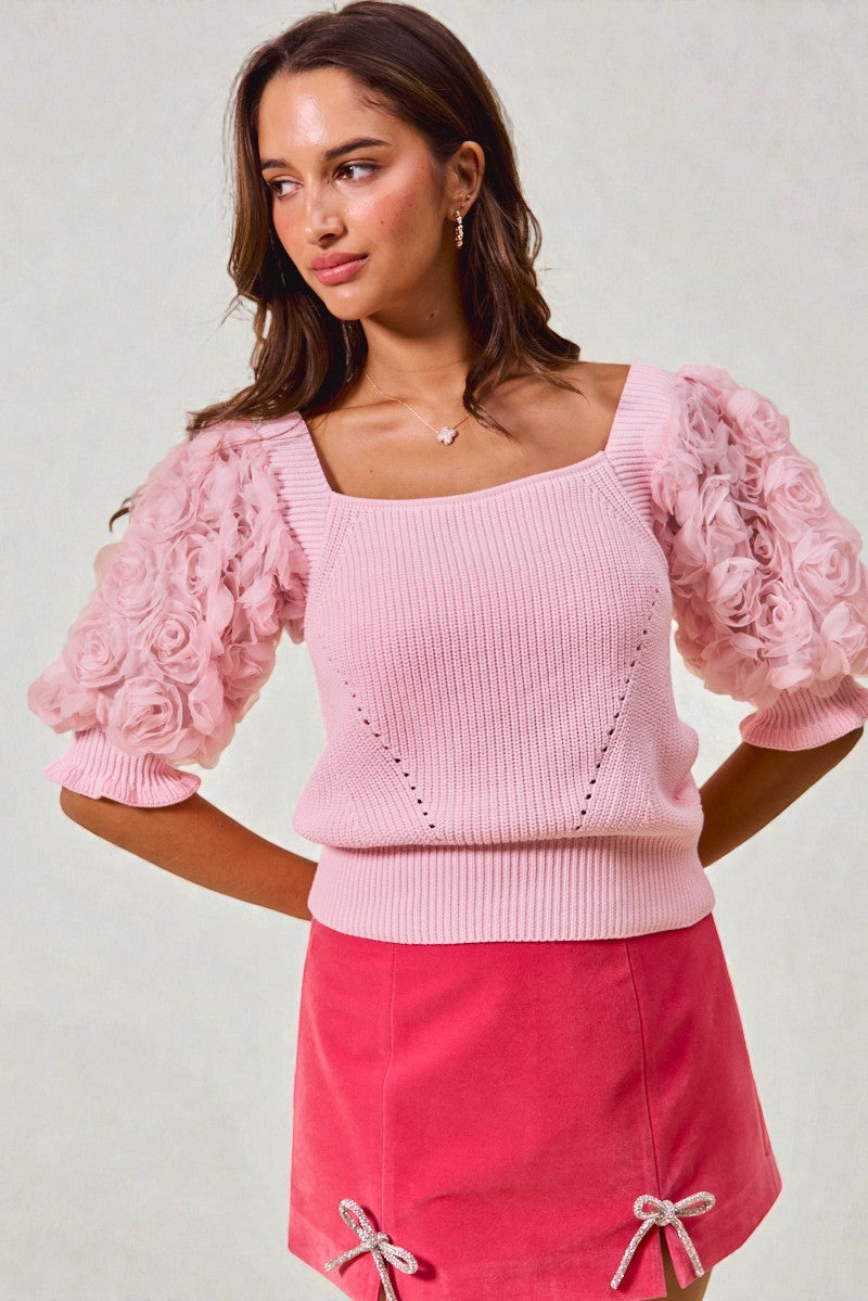 Woman wearing a pink sweater with floral sleeves against a plain background