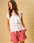 Woman wearing a white lace top and red checkered shorts against a beige textured wall.