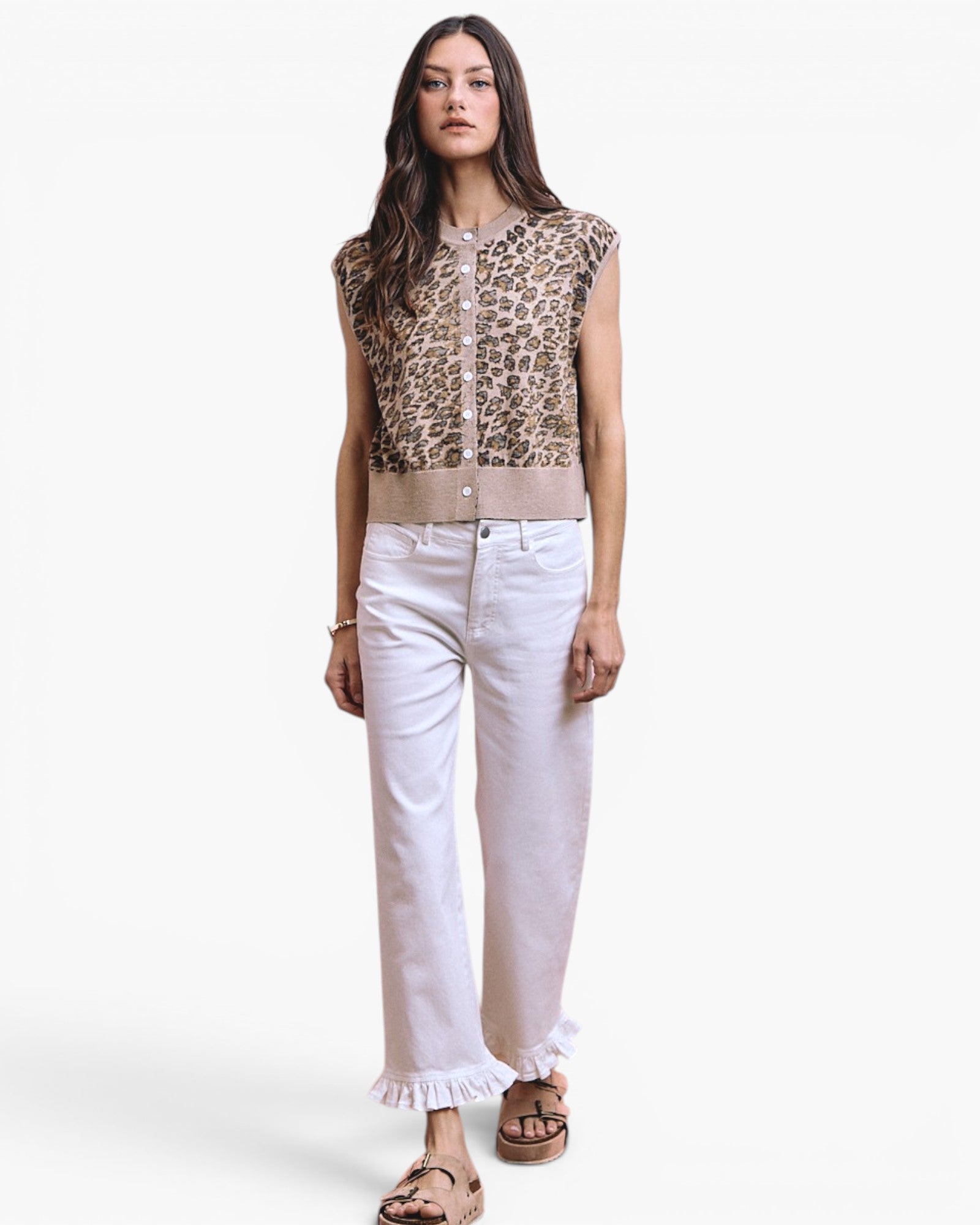A woman modeling a sleeveless leopard-print top with a beige waistband, paired with white cropped jeans featuring ruffled hems and brown sandals, against a plain white studio background.