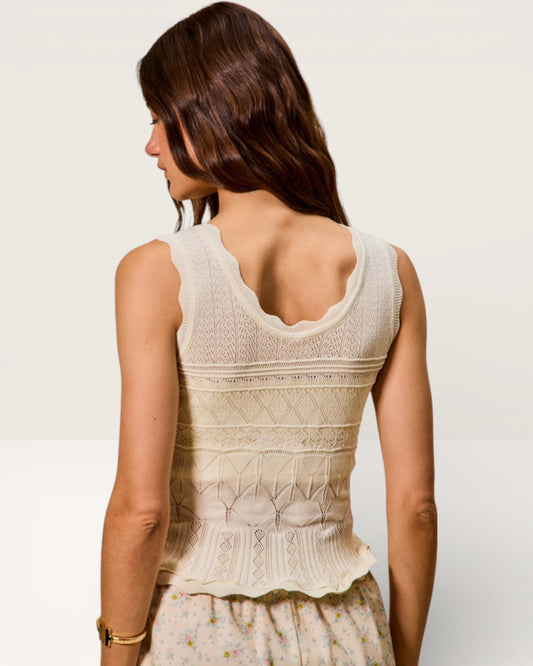 Woman wearing a beige sleeveless top with a subtle pattern on a plain background