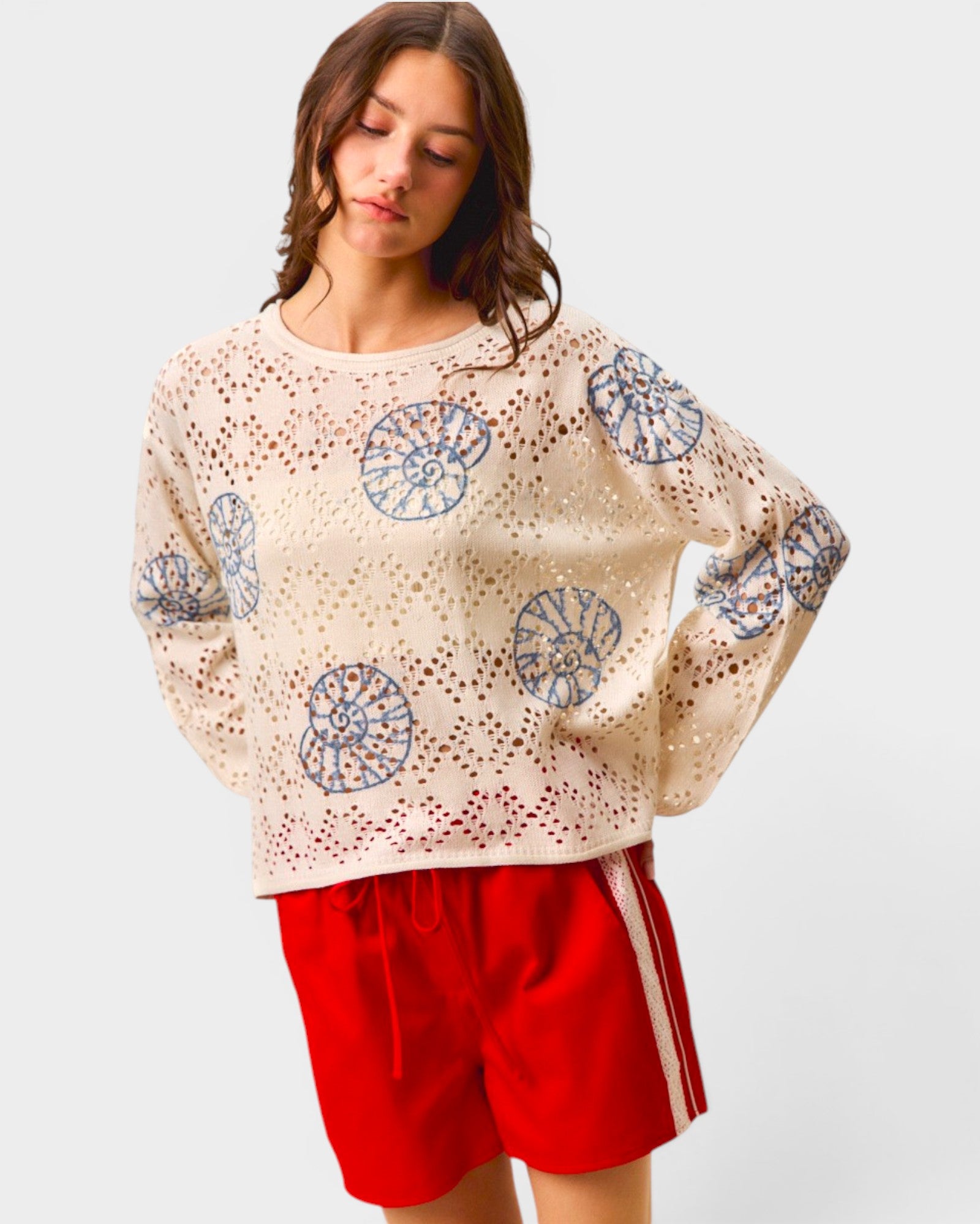 Woman wearing a cream sweater with blue patterns and red shorts on a light gray background