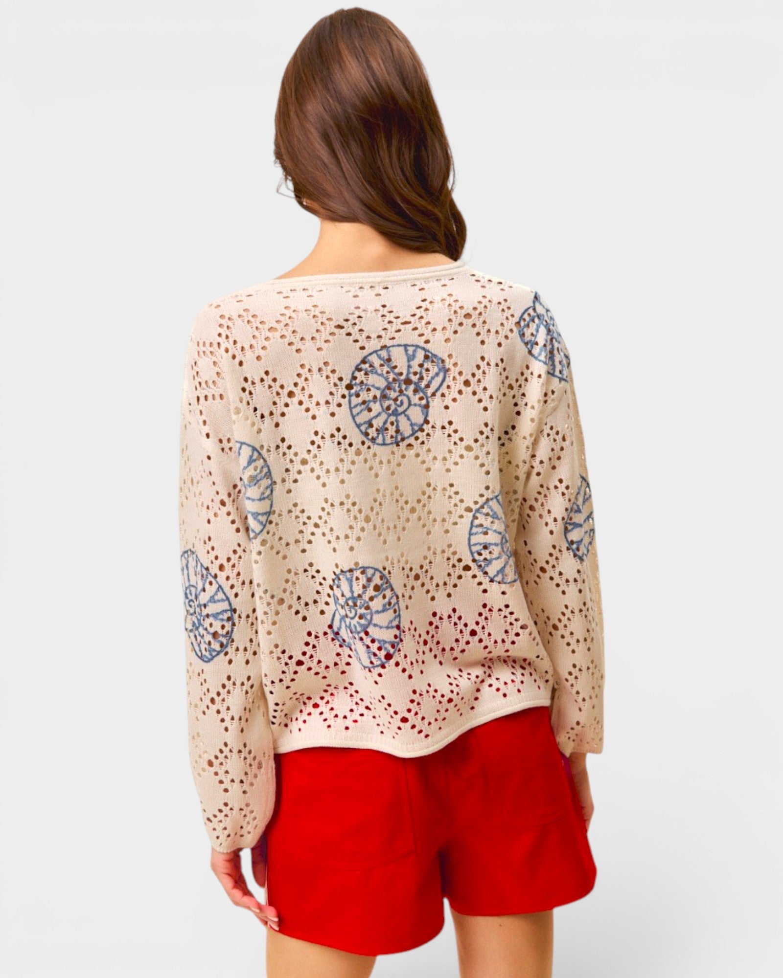 Woman wearing a beige embroidered top and red shorts on a white background