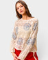 Woman wearing a beige sweater with blue floral patterns on a white background