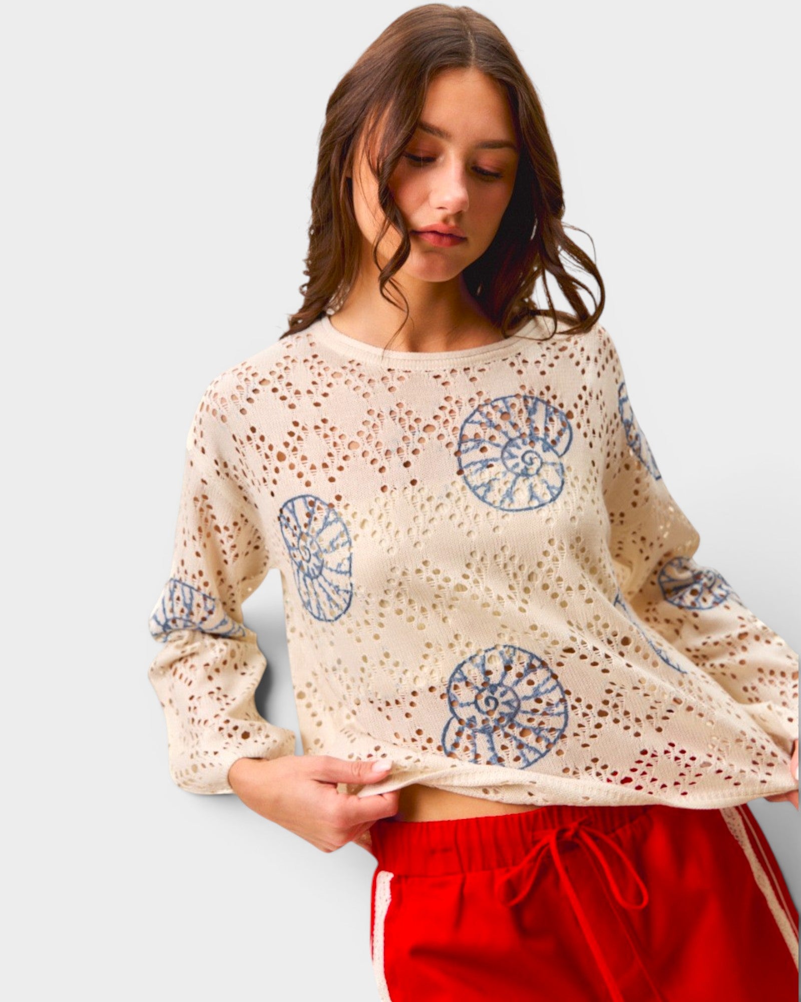 Woman wearing a beige sweater with blue patterns and red pants on a light gray background