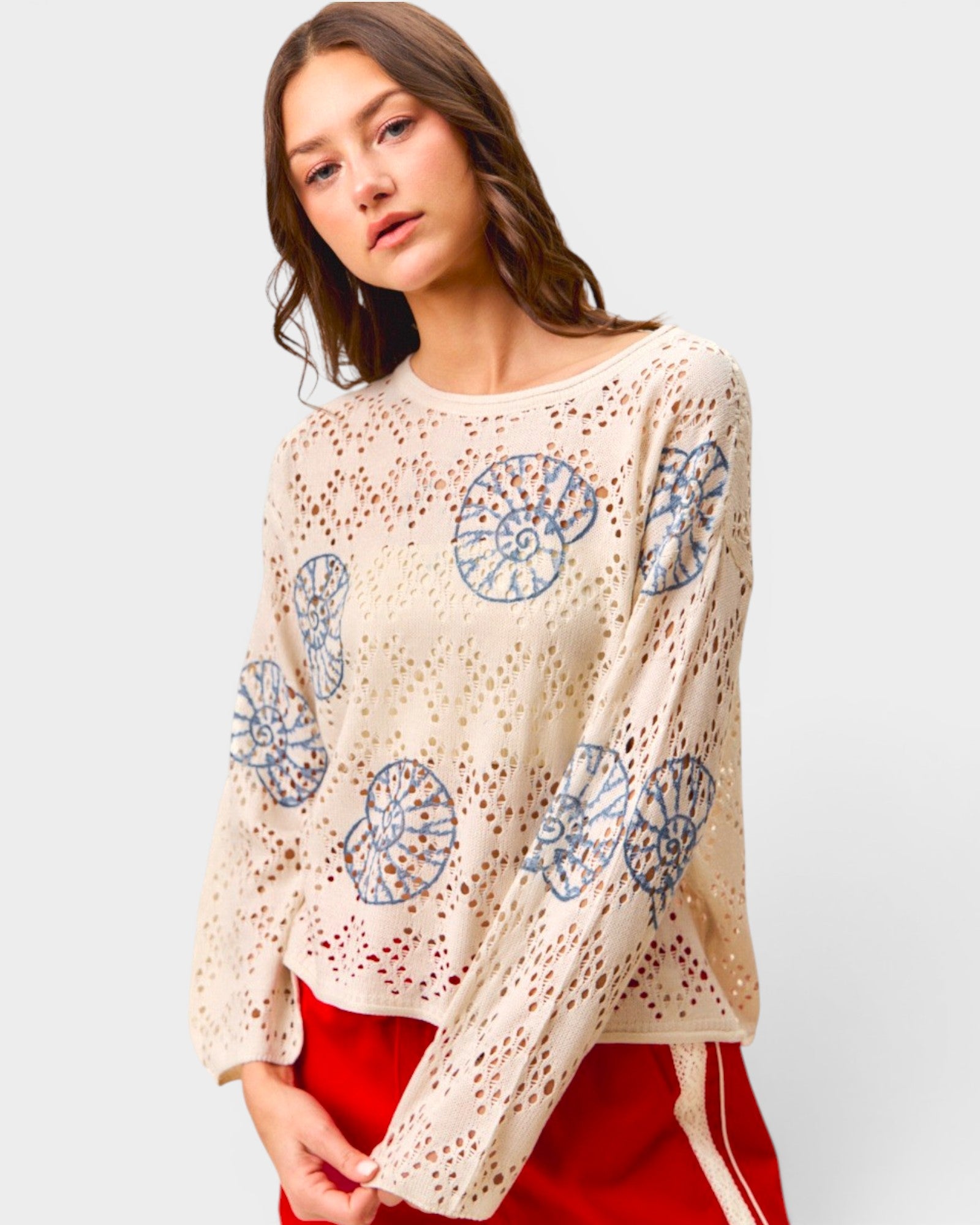 Woman wearing a beige sweater with blue floral patterns on a white background