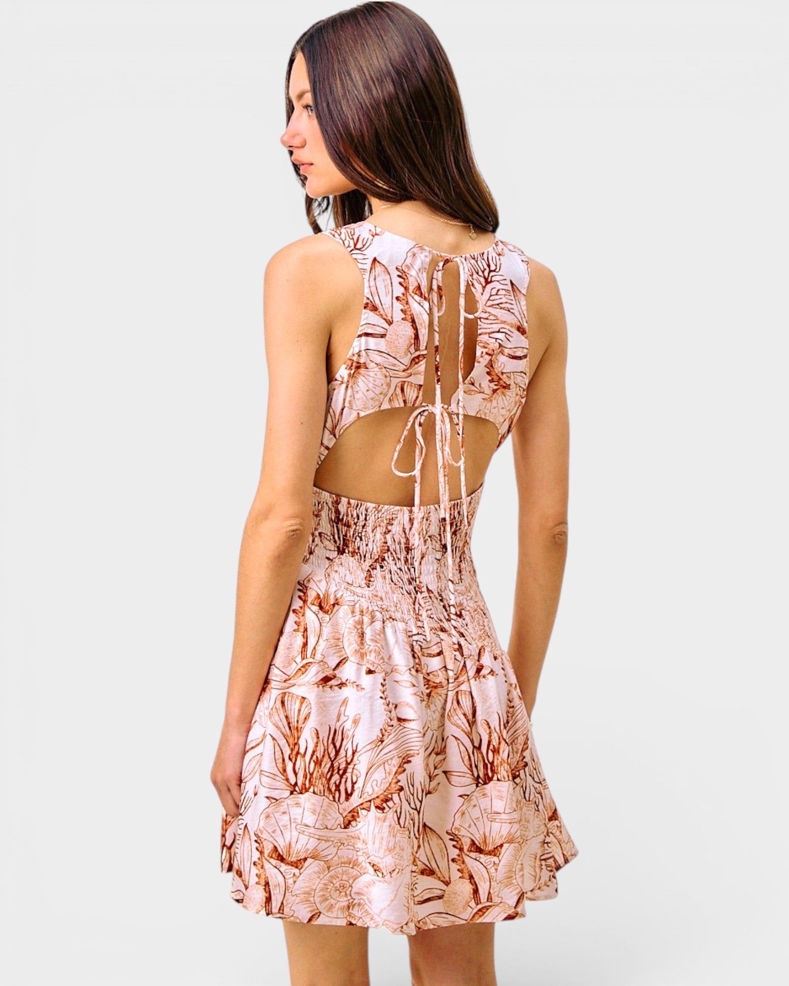 Woman wearing a floral dress with cut-out back on a plain background