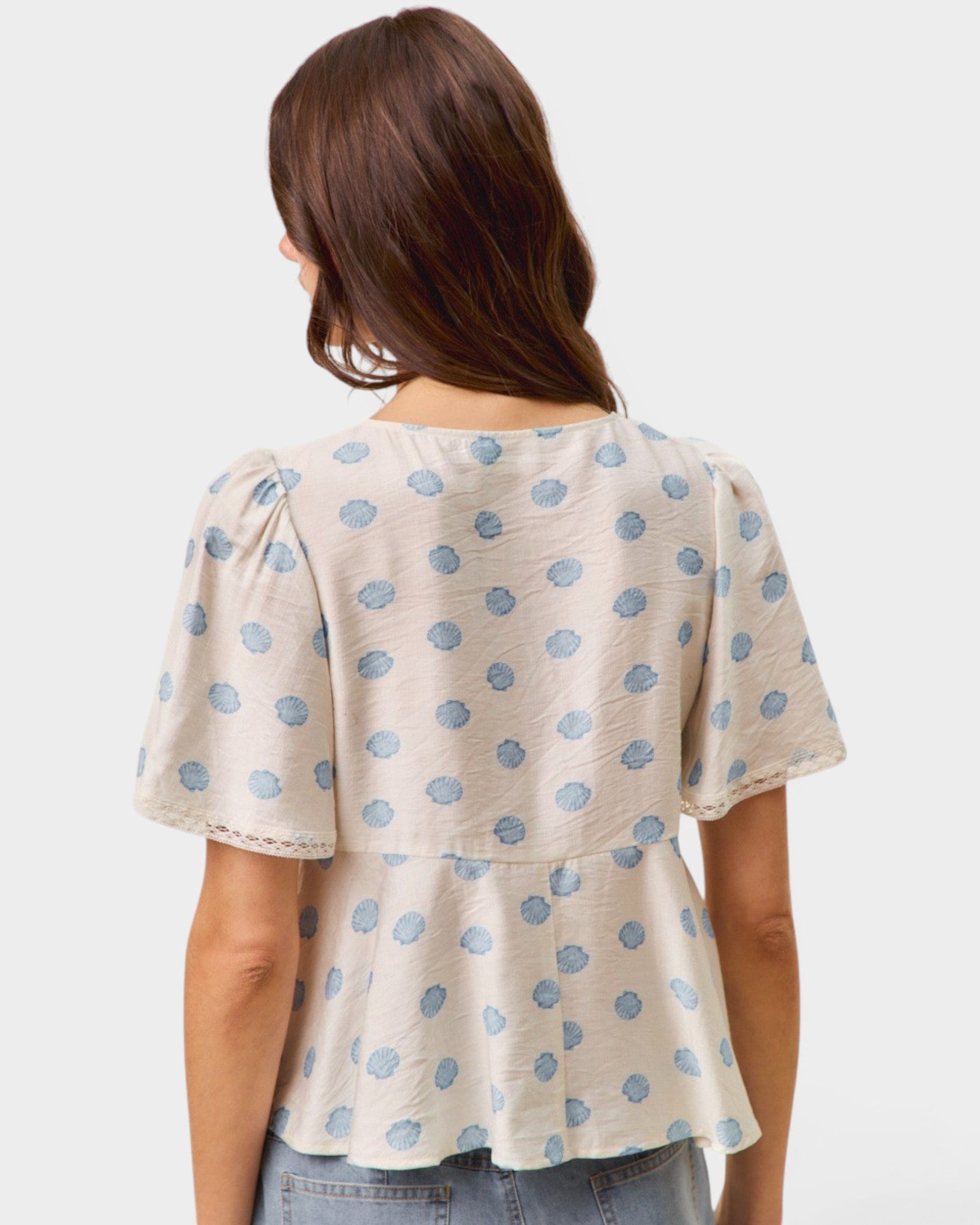 Woman wearing a polka dot blouse with short sleeves on a plain background
