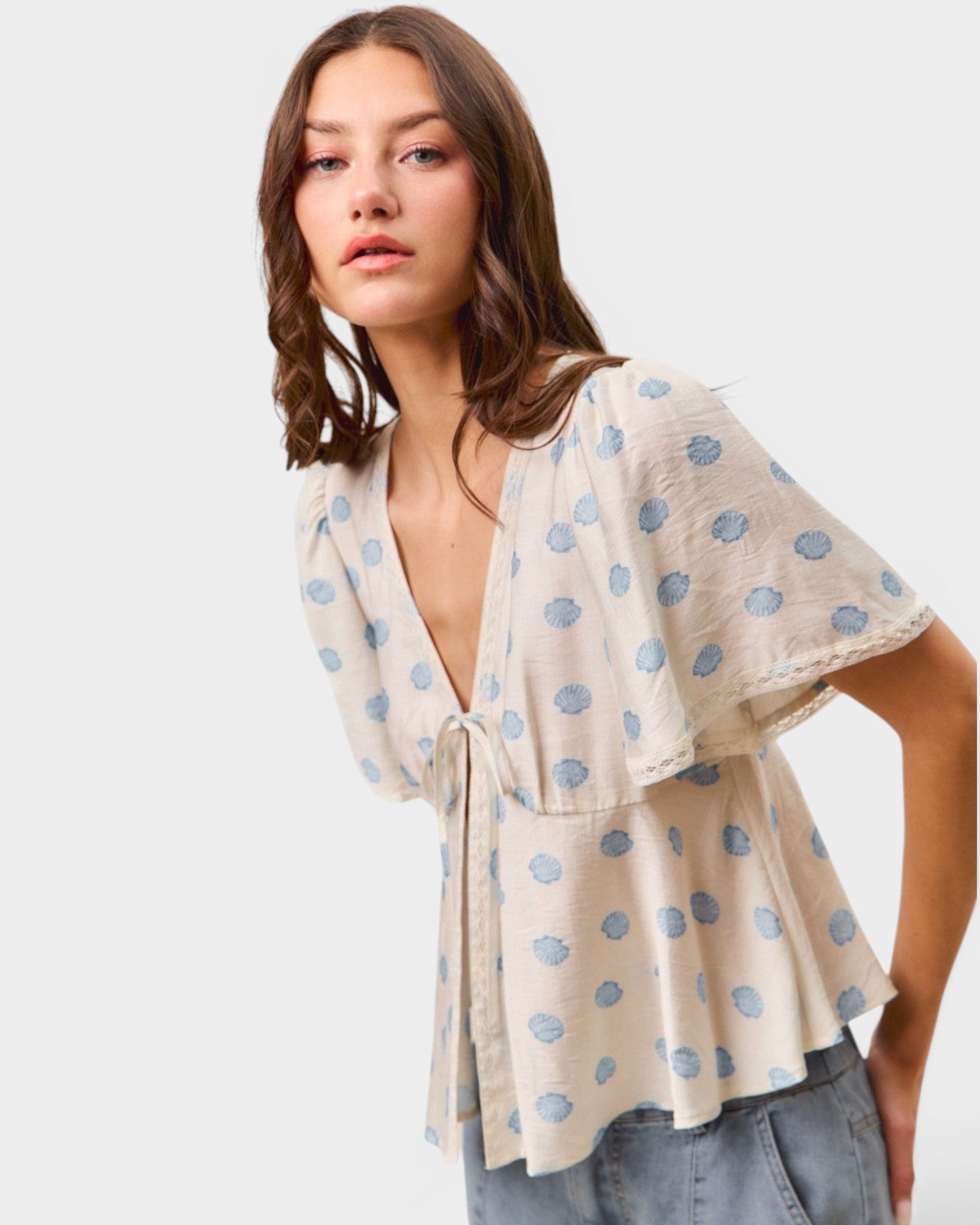 Woman wearing a beige kimono-style top with blue floral patterns on a white background