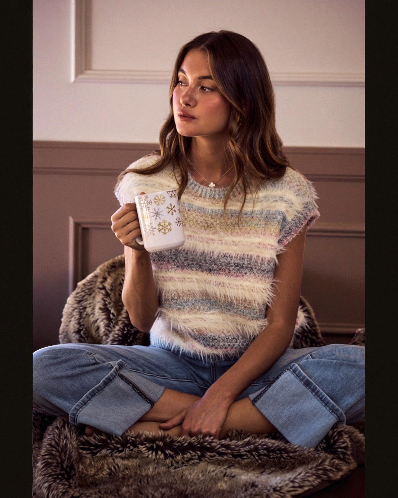 Woman sitting on a fur rug holding a mug with a floral design.