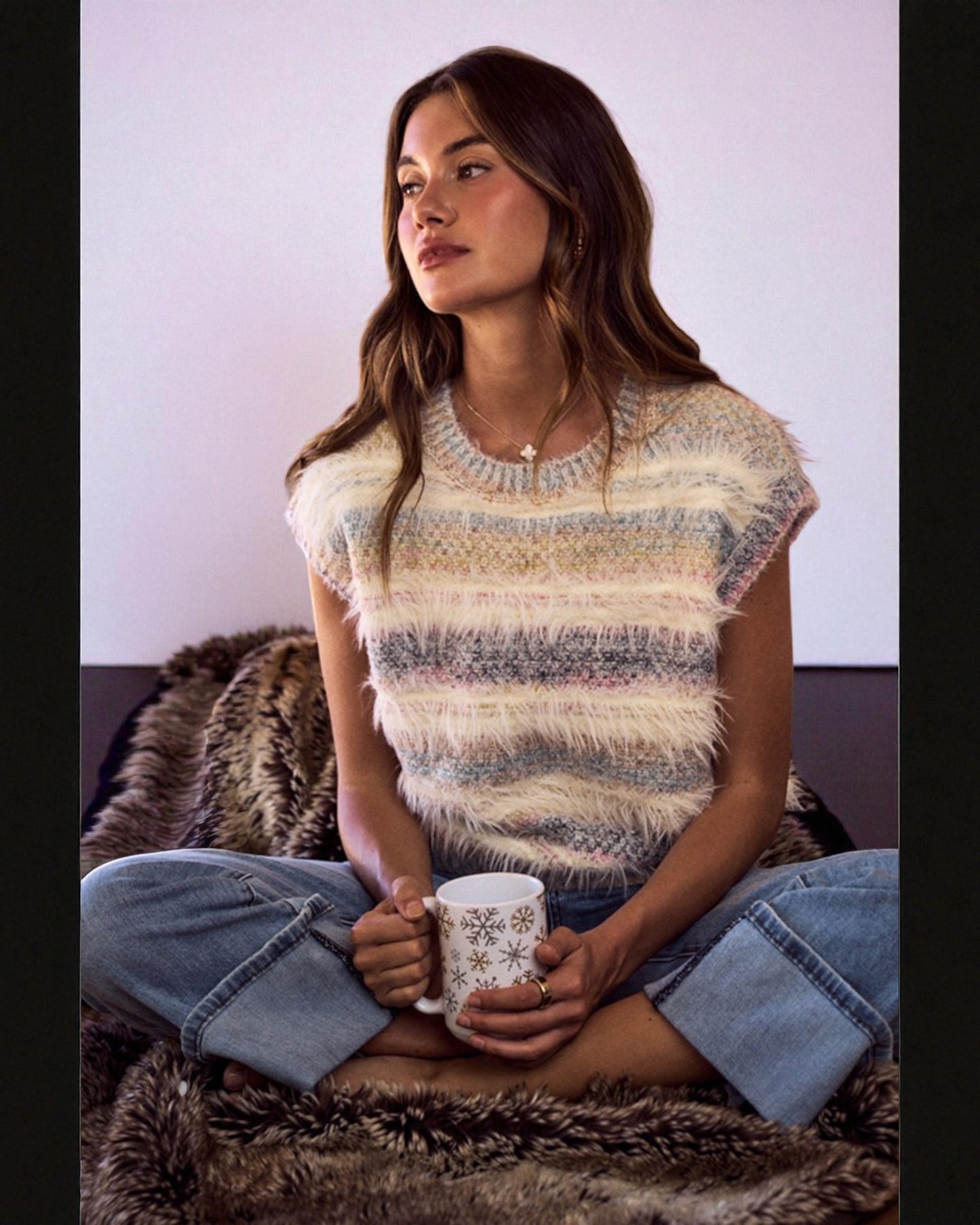 Woman wearing a striped sweater and holding a mug, sitting on a textured surface.