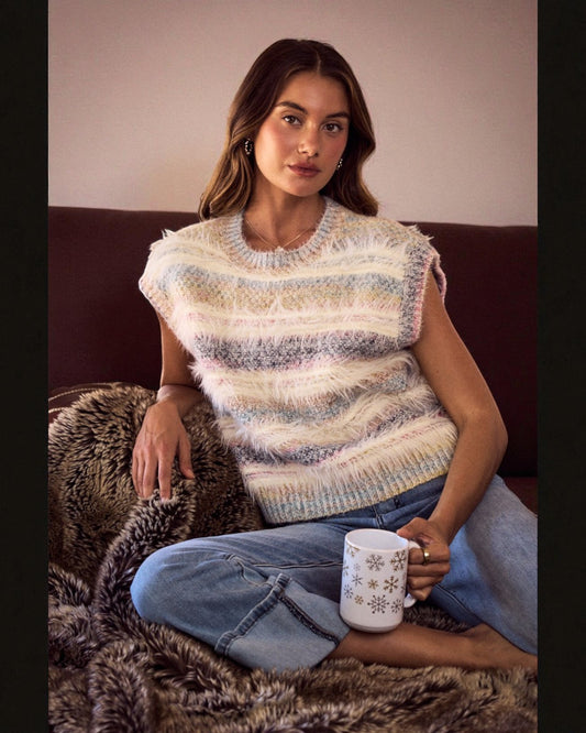 Woman wearing a striped sleeveless sweater sitting on a couch with a mug.