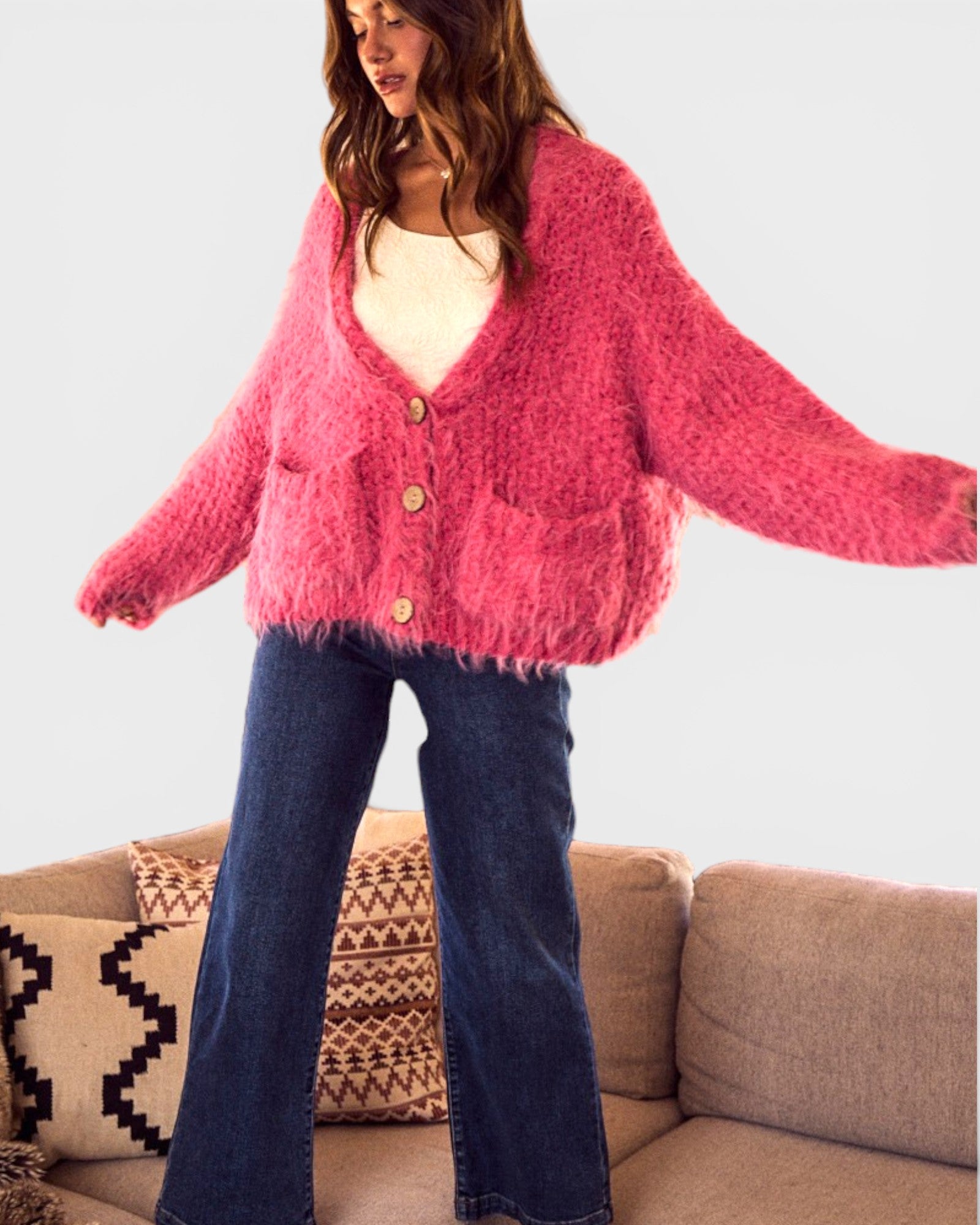 Person wearing a pink cardigan and blue jeans standing in front of a beige couch with patterned cushions.