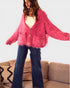 Person wearing a pink cardigan and blue jeans standing in front of a beige couch with patterned cushions.