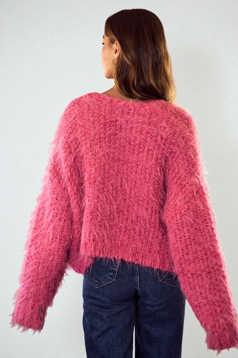 Person wearing a pink fuzzy sweater and blue jeans against a white background