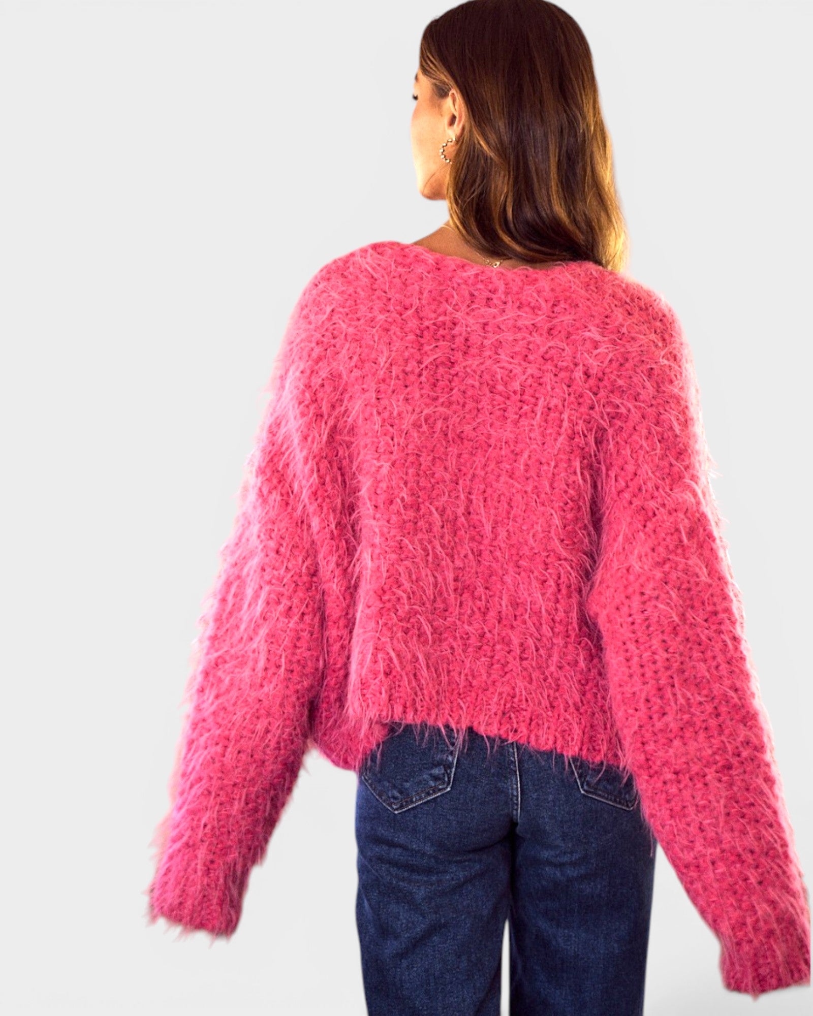Person wearing a pink fuzzy sweater and blue jeans on a white background