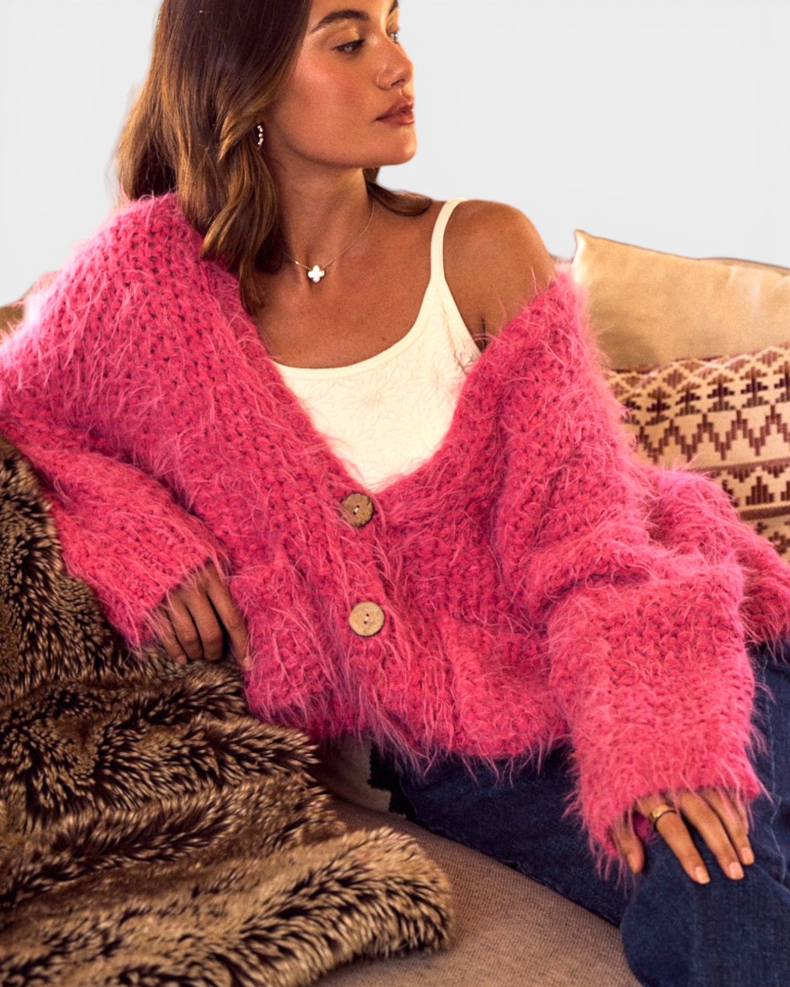 Woman wearing a pink fuzzy cardigan sitting on a couch.