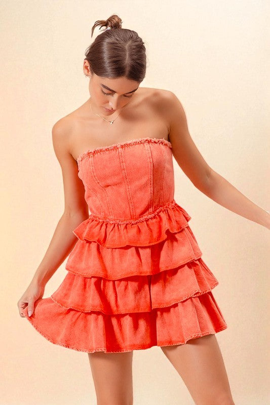 Woman wearing a coral strapless dress with ruffled layers on a beige background