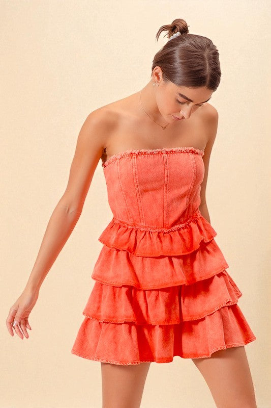 Woman wearing a coral strapless dress with ruffled layers on a beige background
